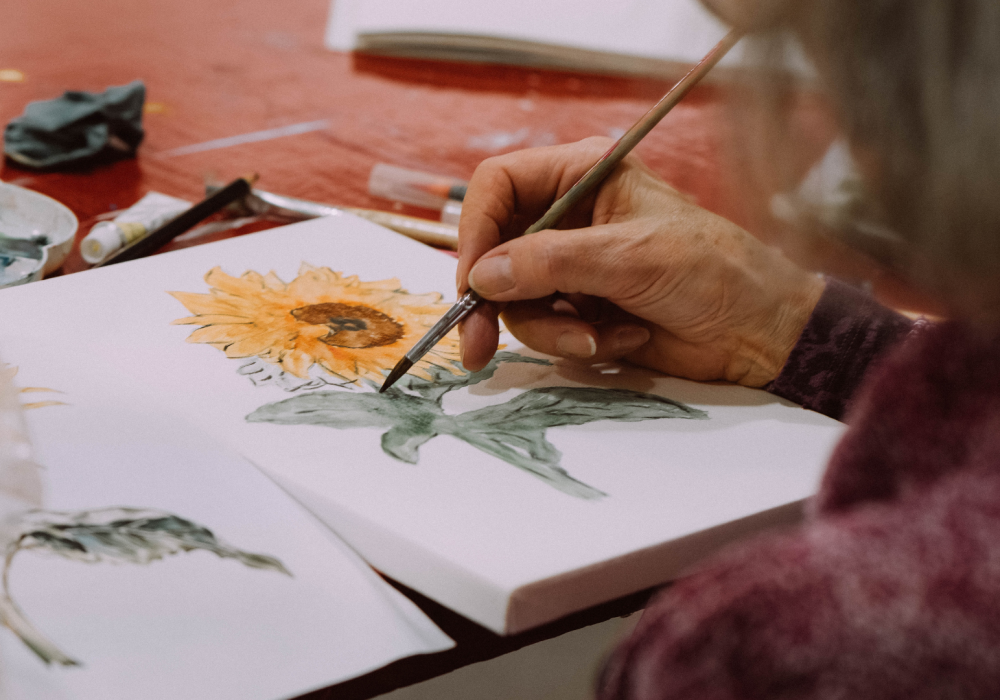 A close up of a hand painting a yellow sunflower.