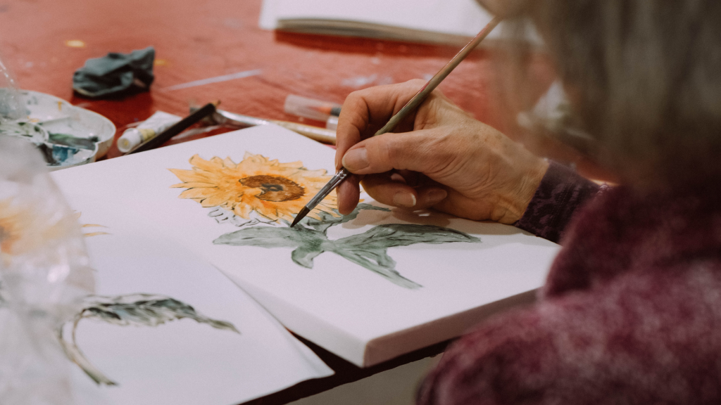A close up of a hand painting a yellow sunflower.