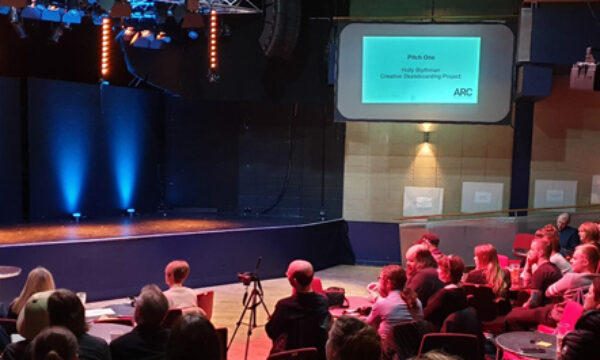 A person stands behind a lectern, pitching their project idea to an audience in The Point at ARC.