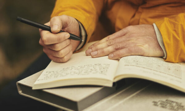 A person sits writing in an open notebook