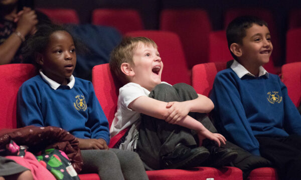 Three children seat in theatre seats enjoying a performance
