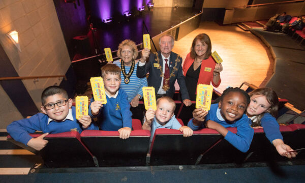 A group of children and adults hold up bright yellow theatre tickets