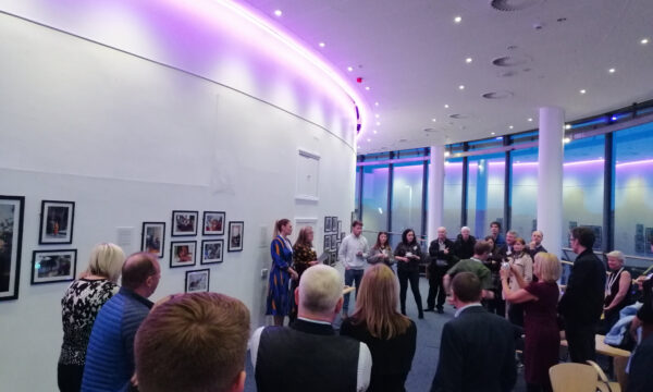 A crowd of people gathered in a gallery to view artwork lining the walls