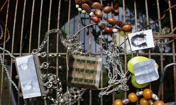 A selection of beads, other jewellery and photographs (of people) lie on a metal grille over water.