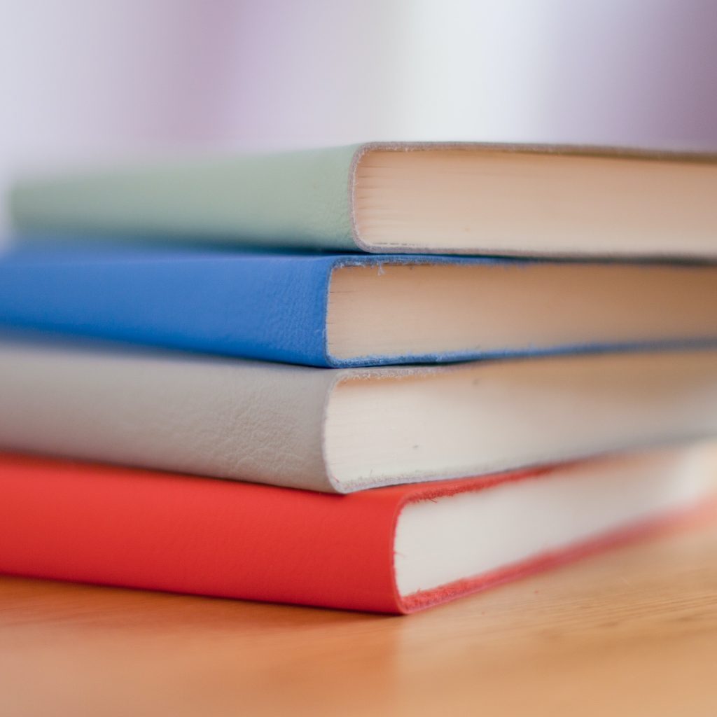 A stack of colourful notebooks on a wooden table.