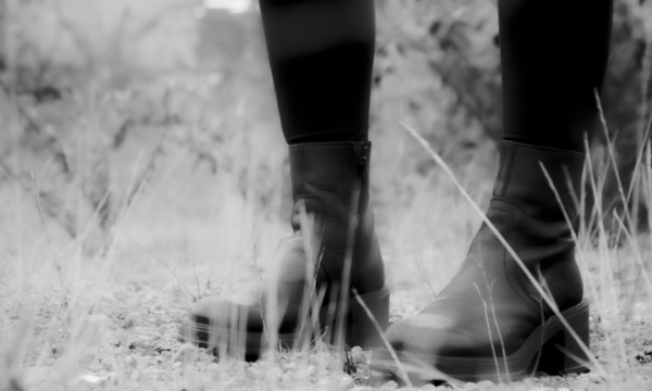 A black and white image of a person's lower legs and feet (wearing black boots).