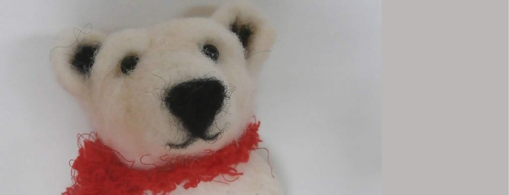 A felt polar bear wearing a red scarf, on a white background