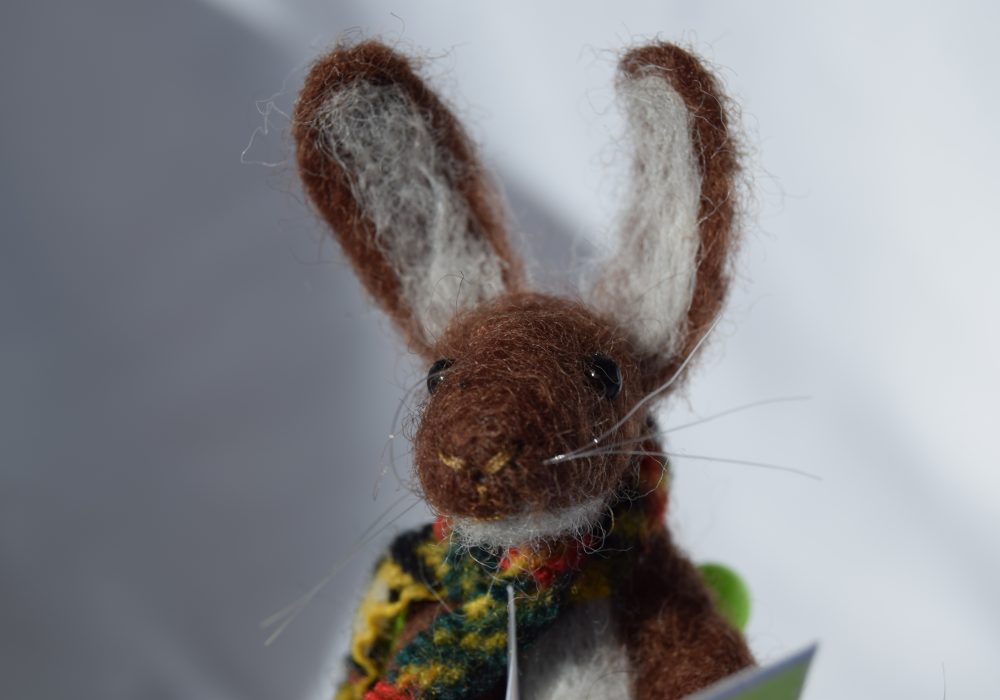 A felt brown hare, wearing a multicoloured scarf, on a white background.
