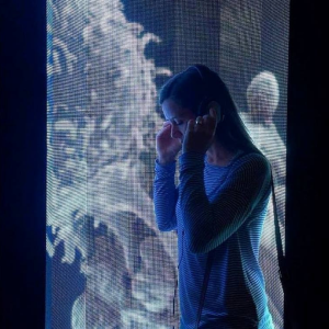 A person standing and wearing headphones against the background of an art installation.