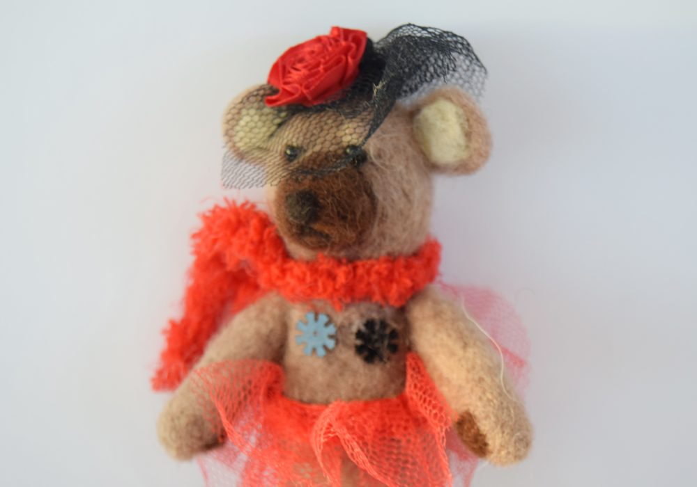 A needle felt sculpture of a brown bear, wearing a black and red burlesque style outfit.