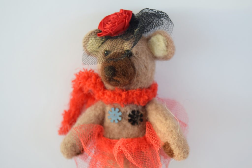 A needle felt sculpture of a brown bear, wearing a black and red burlesque style outfit.