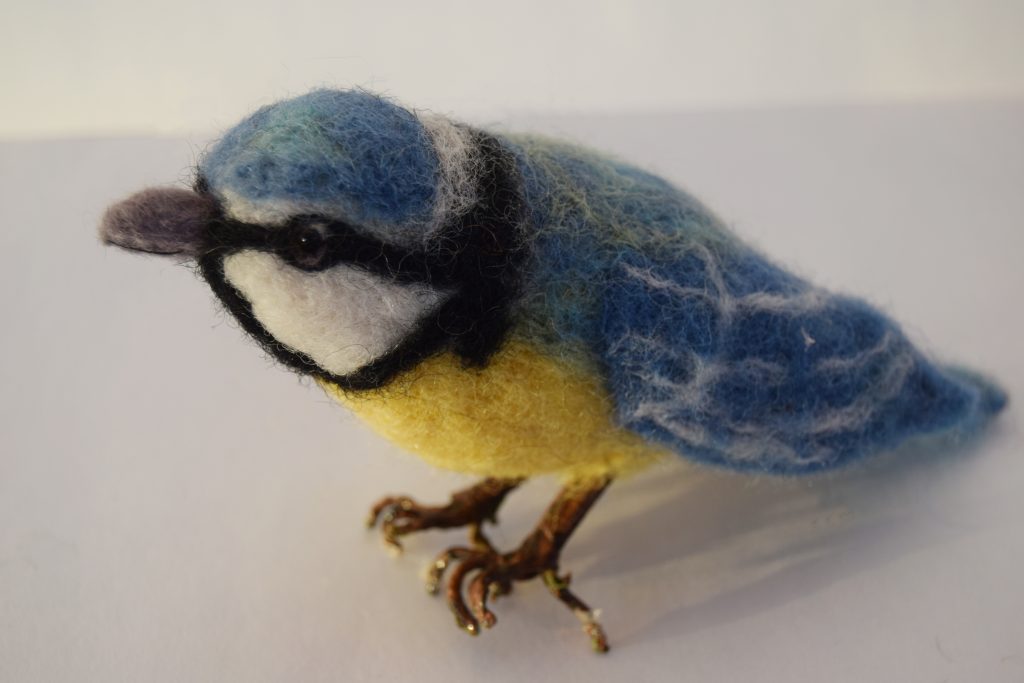 A needle felt sculpture of a blue and yellow bird