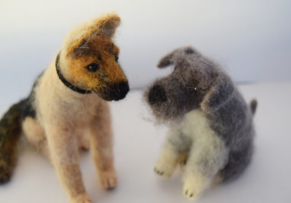 Two needle felt dog sat side by side, on the left is a german shepherd wearing a black collar, and on the right is a grey schnauzer.