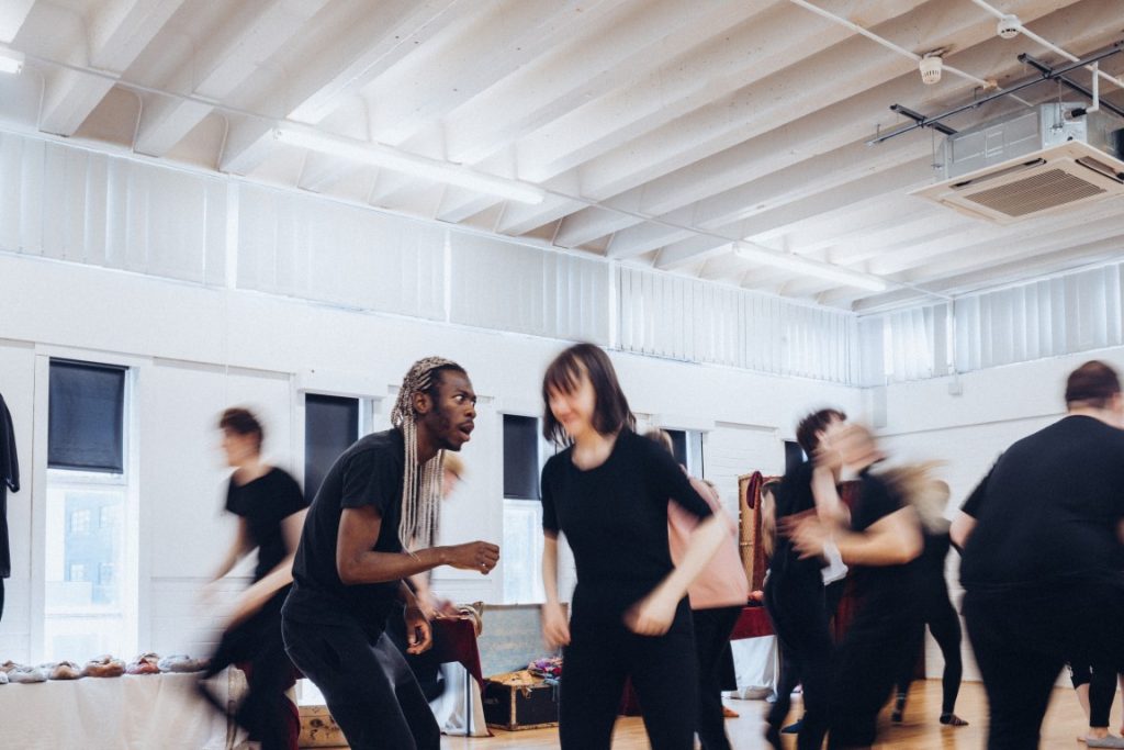 An image of a room full of students working on a piece. Some figures are blurred to show movement.