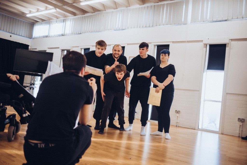 A group of students (all dressed in black) pose for a photographer in front of them.