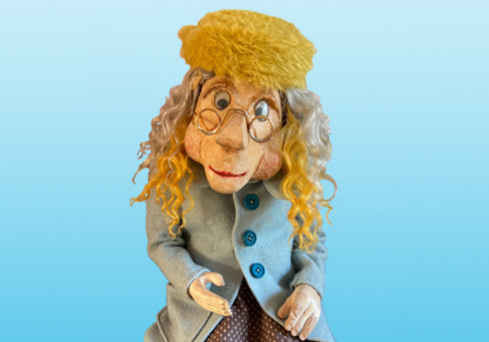 Puppet of the old lady 'Oldilocks', wearing a yellow hat, small round glasses and a pale blue wool coat