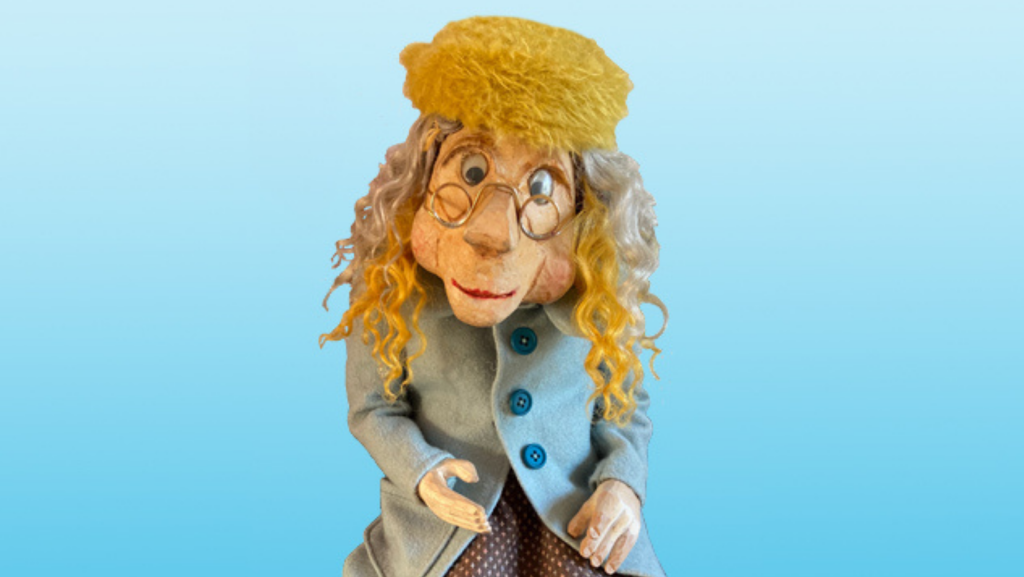 Puppet of the old lady 'Oldilocks', wearing a yellow hat, small round glasses and a pale blue wool coat