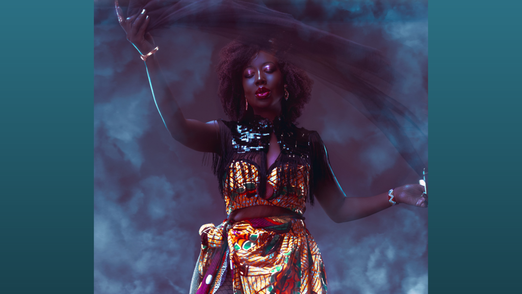 Shot of artist Radikal Queen in a brightly coloured dress, surrounded by a cloud of dry ice