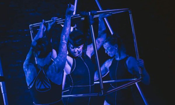 3 members of Uncaged Aerial Theatre in and around a square metal 'cage'