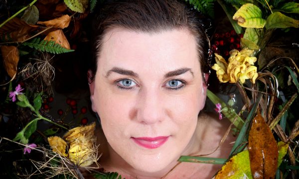 Headshot of poet Kate Fox, she is surrounded by foliage.