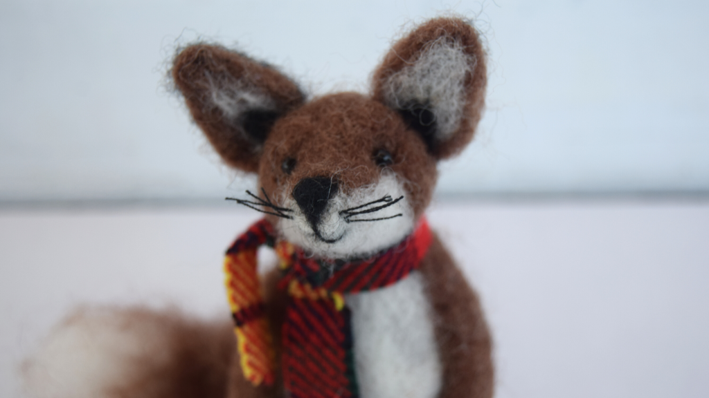 A needle felt fox in a red tartan scarf