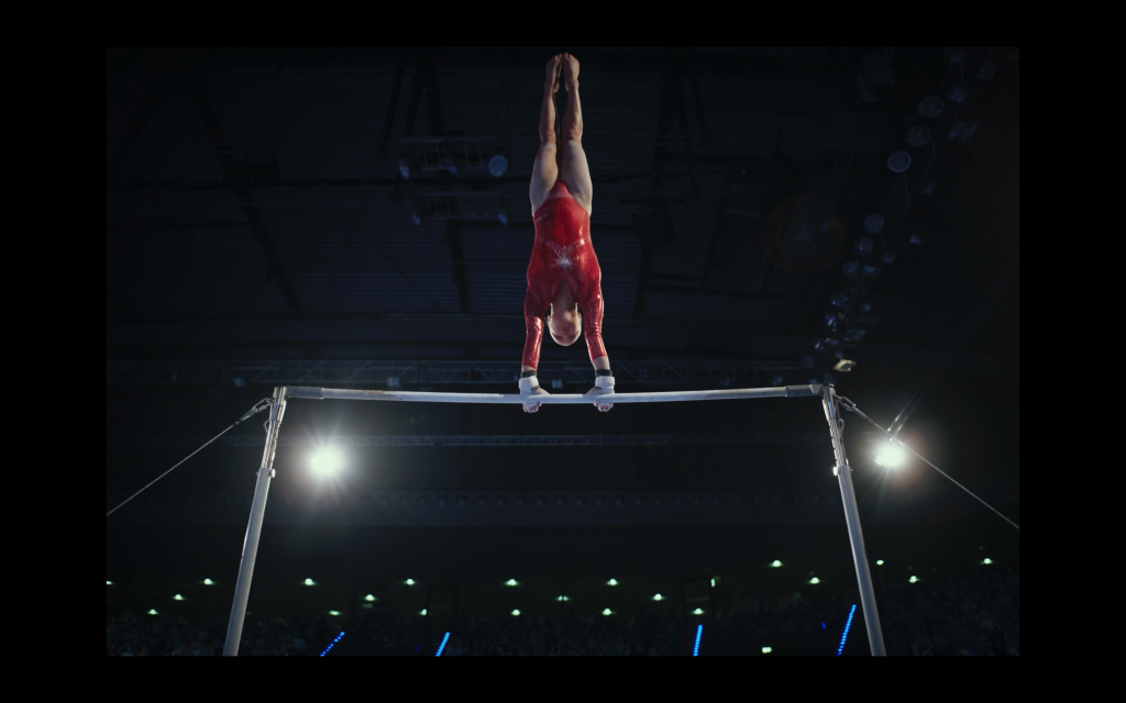 Actor playing Olga wearing a red leotard on gymnastic bars