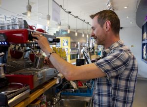 A member of staff standing behind the No 60 bar making a coffee with the coffee machine