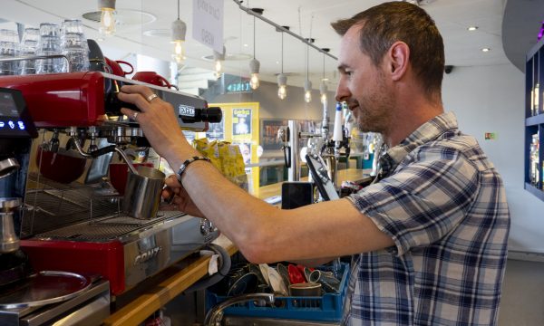 A member of staff standing behind the No 60 bar making a coffee at the coffee machine