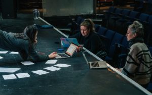 Three people gathered around notes and laptops during rehearsals in ARC's Theatre