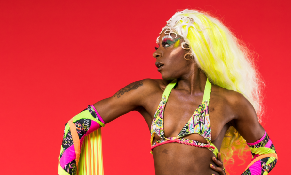 Performer Symoné in a brightly coloured bikini style costume, with a long yellow wig