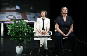 Two seated performers on the stage of Dead Cats. Next to them is a large plant.