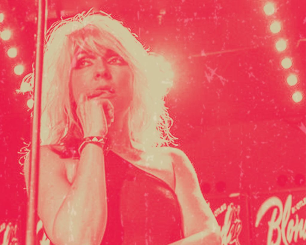 Bootleg Blondie frontwoman Debbie Harris stands in the centre of the image, only her head and shoulders are visible. She is looking off to the left of the camera, with her hand up against her mouth. The image has a red overlay.