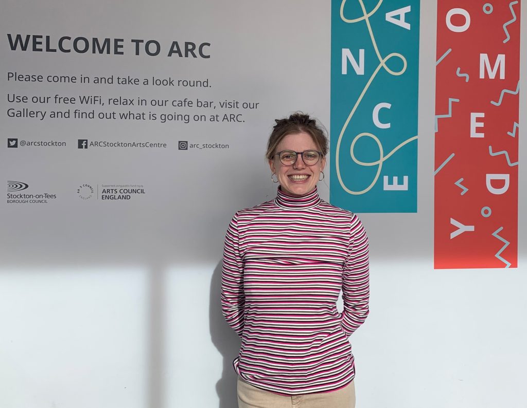 Cristina smiles for the camera in ARC's foyer, standing in front of the 'WELCOME TO ARC' sign