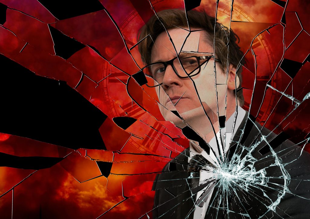 Comedian Ed Byrne looks intensely at the camera, in front of him looks like shattered glass.