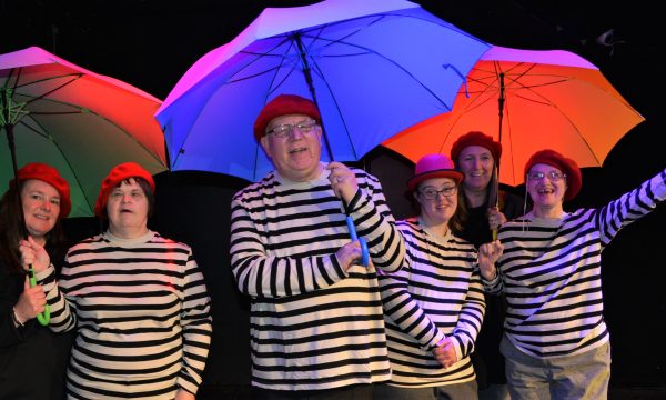 Performers from Full Circle, wearing matching striped tops, hold blue and red umbrellas
