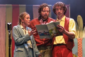 Production shot - 3 performers gathered around the book of Dinosaurs and All That Rubbish