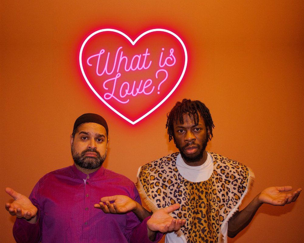 Umar Butt and Alberto Dumba stand side by side. They've both got their arms out, palms up, with questioning looks on their faces. Neon text reading 'What is Love' sits inside a neon heart shape.