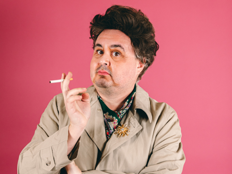 A bright pink background, with Tommy in drag, cigarette in hand.