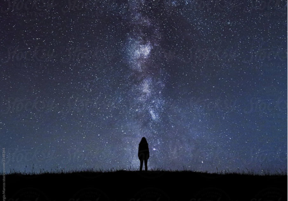 A small figure stands in silhouette against a star-filled night sky