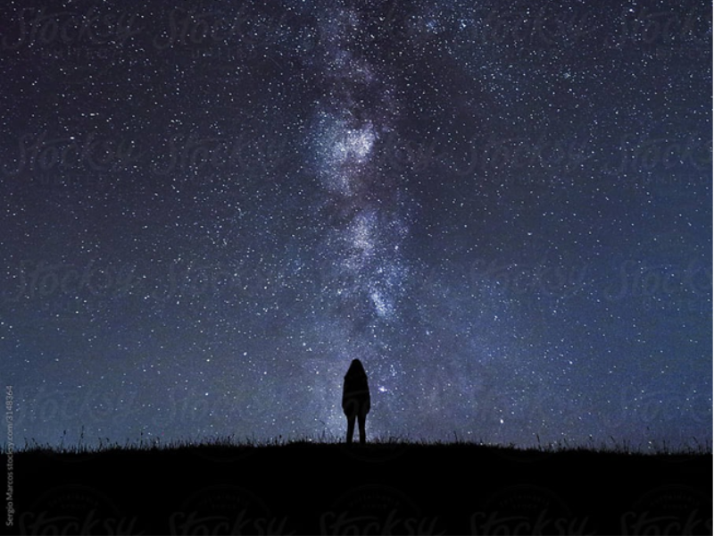 A small figure stands in silhouette against a star-filled night sky