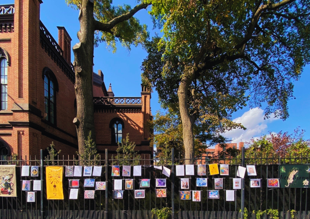 Image of a wide range of artwork on display on the railings outside Flushing Town Hall in New York.