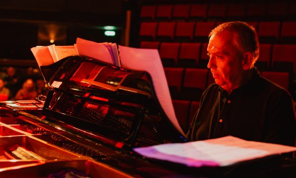 Jeremy sits at a piano on stage