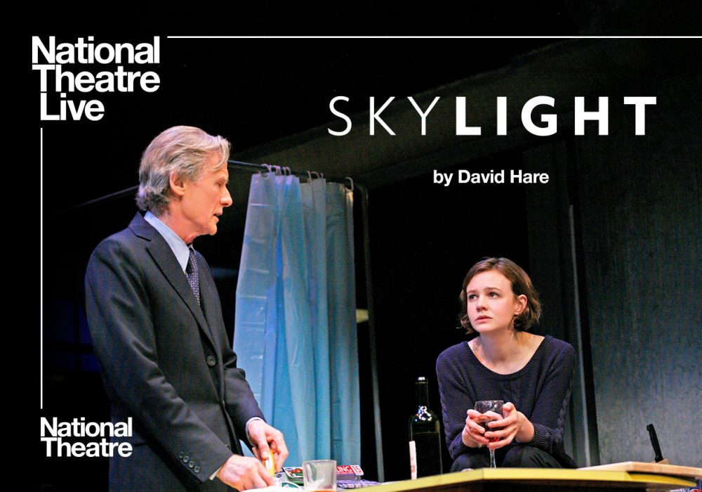 man in a suit stood facing a woman sat with glass of red wine National Theatre Live Skylight