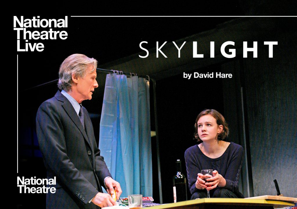 man in a suit stood facing a woman sat with glass of red wine National Theatre Live Skylight