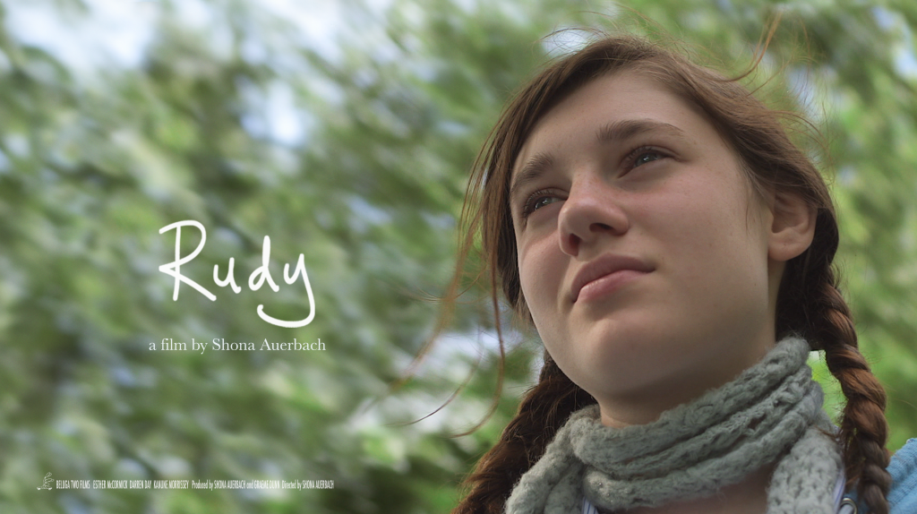 A girl with brown hair in a grey scarf reading Rudy a film by Shona Auerbach