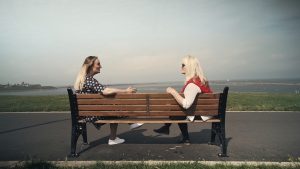 Two women sat on a bench facing each other at the beach