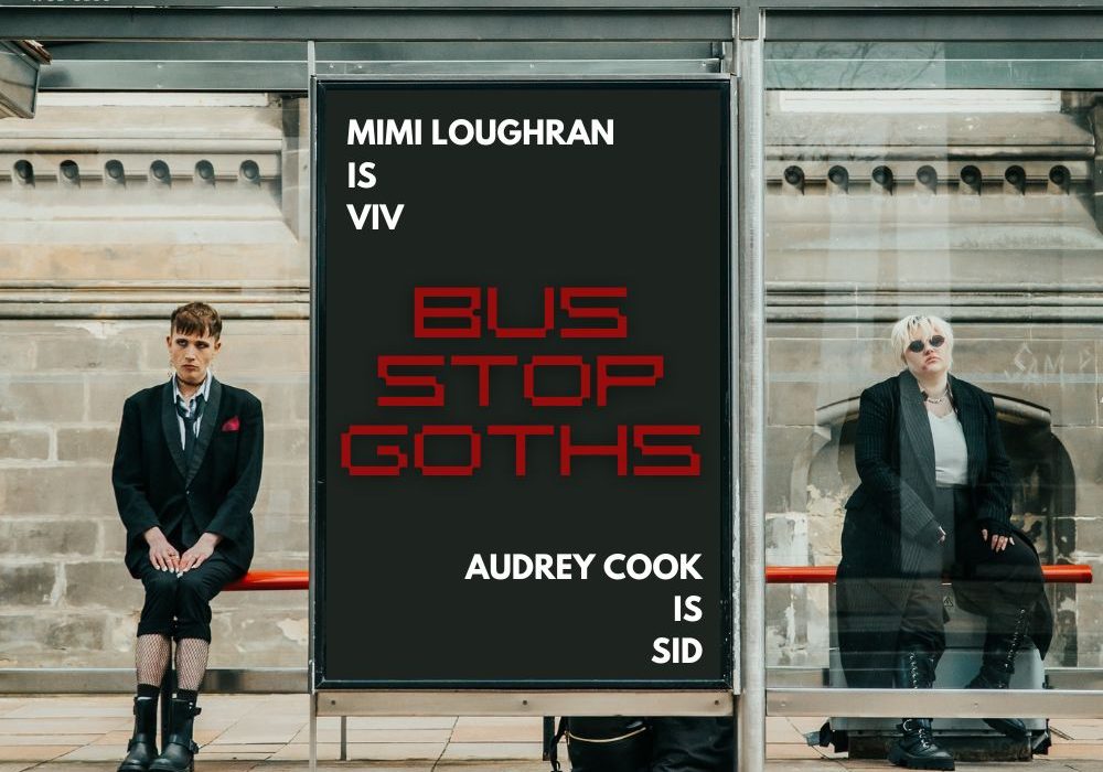 Two people in dark clothes sit at a bus stop on either side of a big advertising banner. The ad reads Mimi Loughran is Viv. Audrey Cook is Sid. Bus Stop Goths.