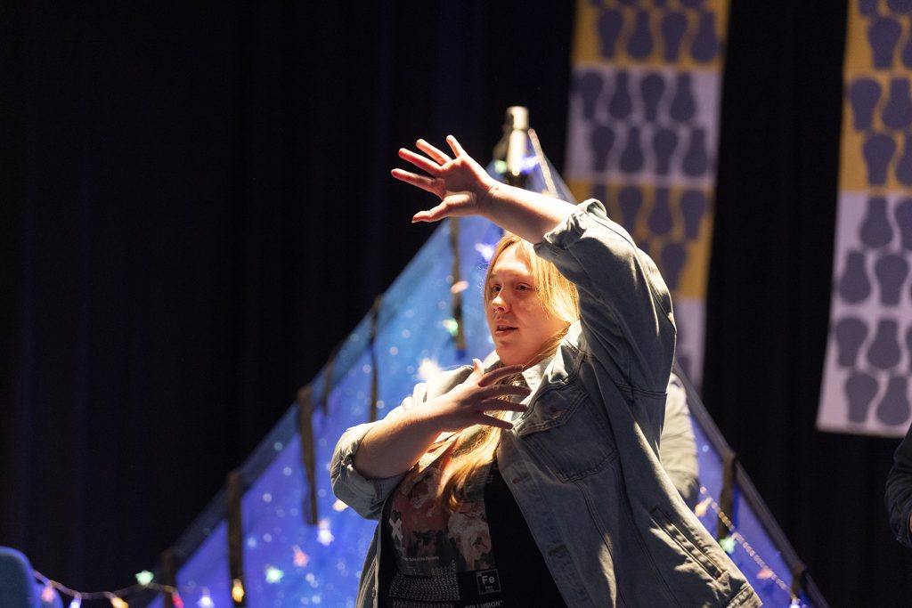 A performer on stage, with a blue tent and fairy lights in the background