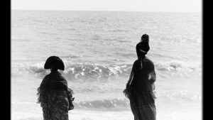 2 West African women stood in front of the sea in black and white