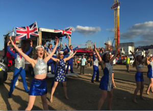 Cheerleaders dressed in blue and silver sequinned outfits holding Union Jack flags.
